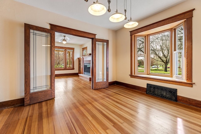 unfurnished room featuring wood-type flooring, baseboards, a glass covered fireplace, and visible vents