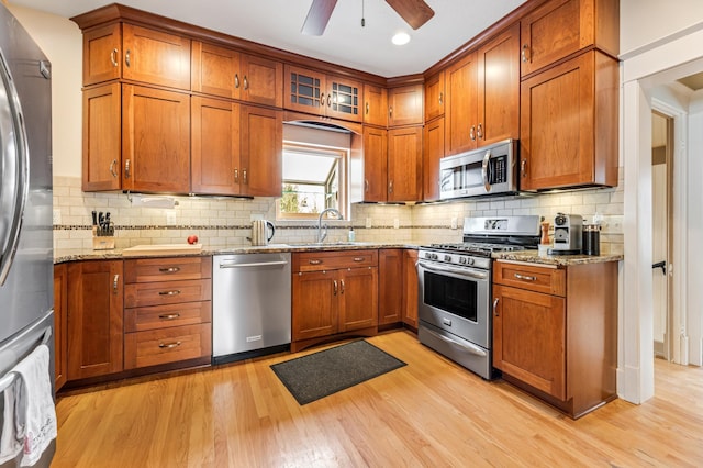 kitchen with brown cabinetry, stainless steel appliances, light wood-type flooring, and a sink