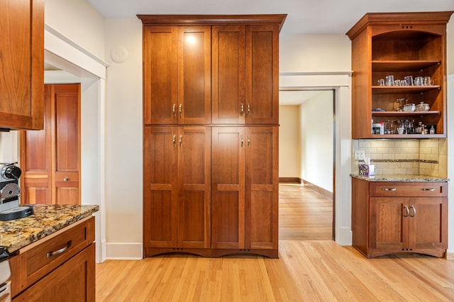 kitchen with light wood-style flooring, baseboards, light stone counters, open shelves, and backsplash