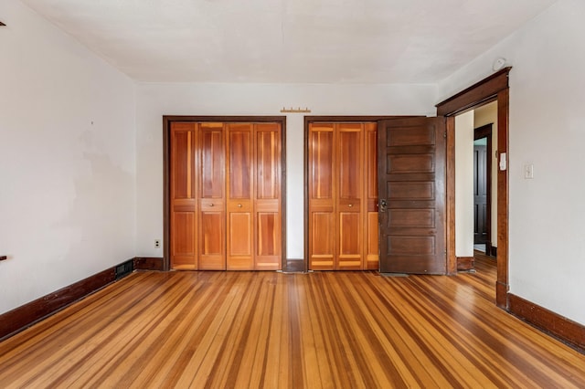 unfurnished bedroom with baseboards, light wood-style floors, and multiple closets