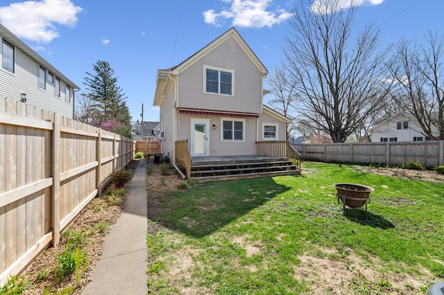 rear view of house with a lawn, a deck, a fire pit, and a fenced backyard