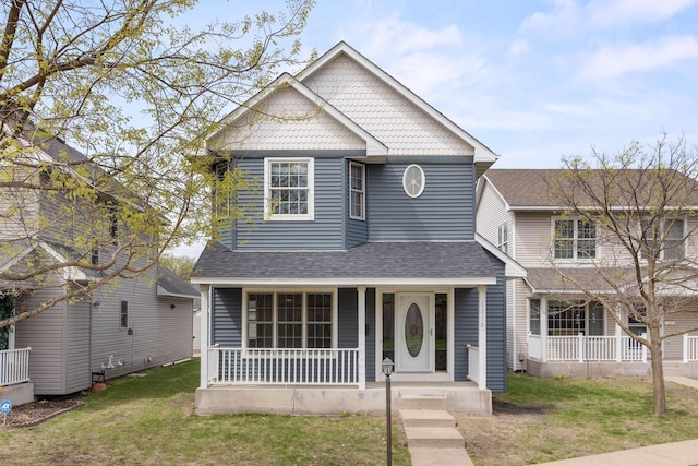 traditional home featuring covered porch, roof with shingles, and a front lawn