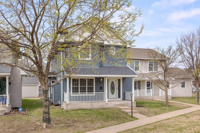 traditional home with covered porch, a shingled roof, and a front yard