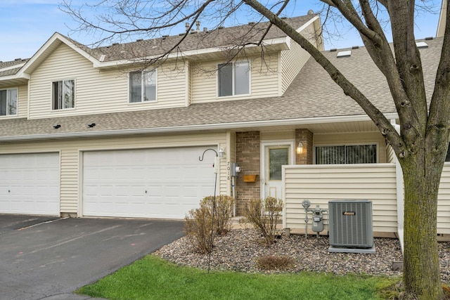 townhome / multi-family property featuring roof with shingles, a garage, aphalt driveway, and central AC