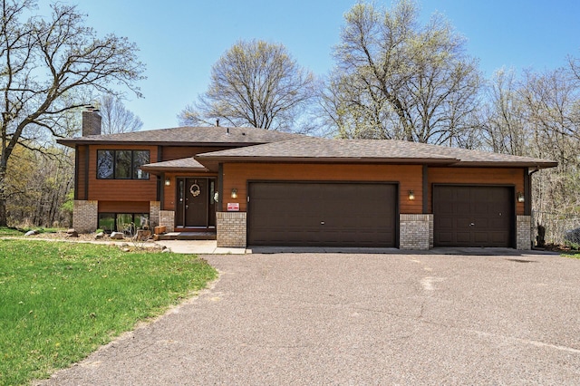 view of front of property featuring aphalt driveway, a garage, a chimney, and brick siding