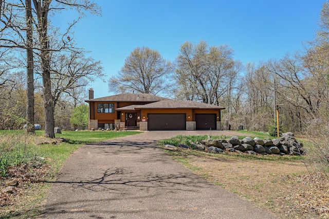 view of front of house with an attached garage, stone siding, a chimney, a front yard, and driveway