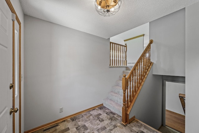 stairway with a textured ceiling, visible vents, baseboards, and stone finish floor