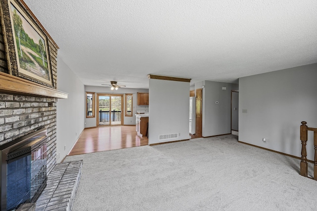 unfurnished living room featuring a textured ceiling, ceiling fan, visible vents, light carpet, and a fireplace