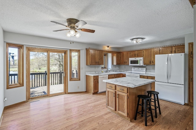 kitchen with a sink, brown cabinetry, white appliances, light countertops, and light wood-style floors