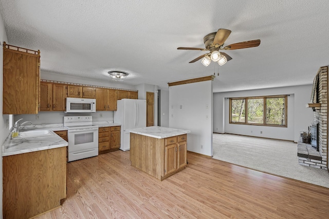kitchen featuring brown cabinets, a sink, open floor plan, a textured ceiling, and white appliances