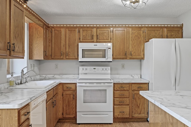 kitchen featuring white appliances, a sink, brown cabinets, light countertops, and light wood-type flooring