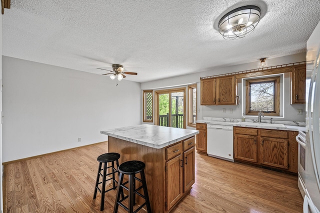 kitchen featuring a sink, brown cabinetry, a textured ceiling, a kitchen breakfast bar, and dishwasher