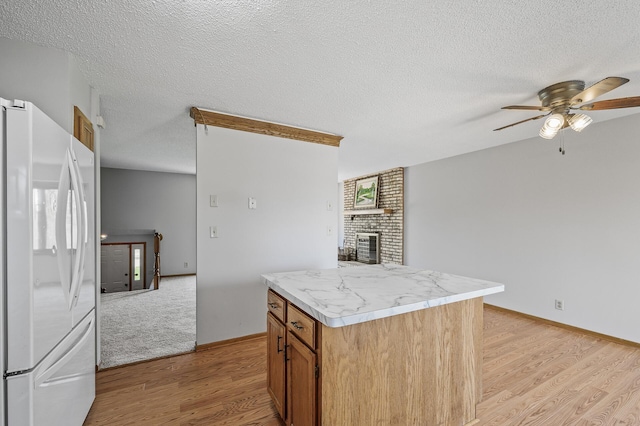 kitchen with freestanding refrigerator, light wood finished floors, a brick fireplace, light countertops, and a ceiling fan
