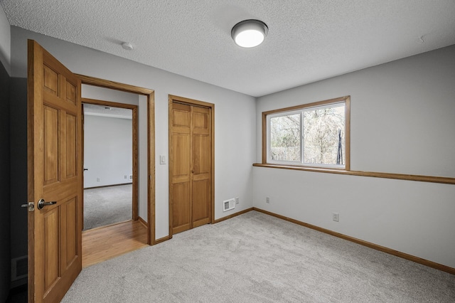 unfurnished bedroom with carpet, a textured ceiling, visible vents, and a closet