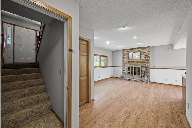 stairs with a textured ceiling, wood finished floors, baseboards, and a brick fireplace