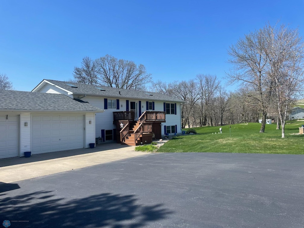 view of front of home with roof with shingles, an attached garage, driveway, a front yard, and stairway