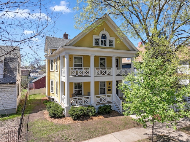 greek revival house featuring covered porch, fence, a chimney, and a balcony