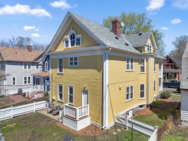 back of house featuring a chimney, a patio area, a shingled roof, and a fenced backyard