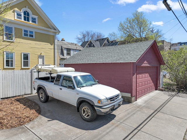 view of side of home with an outdoor structure, roof with shingles, a garage, and fence