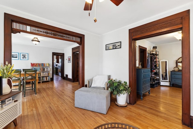 living area with ornamental molding, light wood-type flooring, and ceiling fan