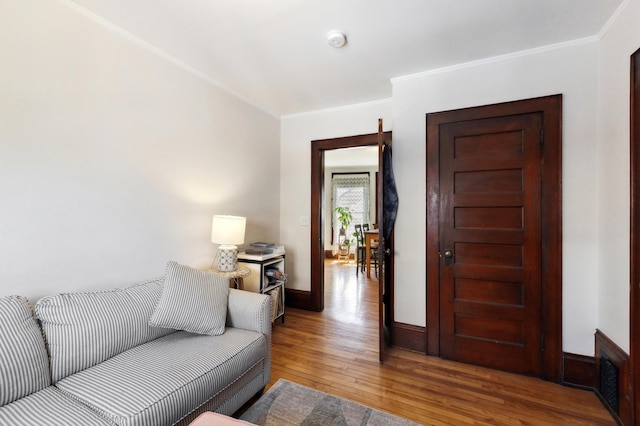 living area with crown molding, visible vents, baseboards, and wood-type flooring