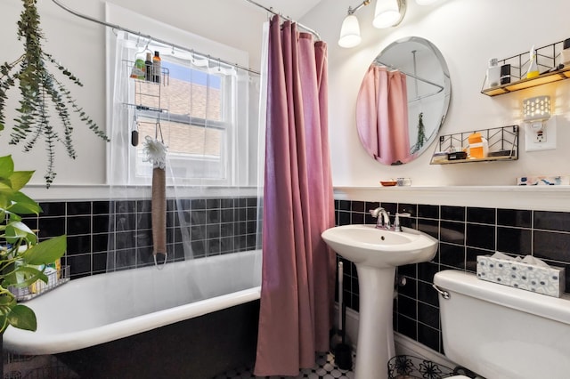 full bath featuring toilet, a sink, shower / tub combo with curtain, tile walls, and wainscoting