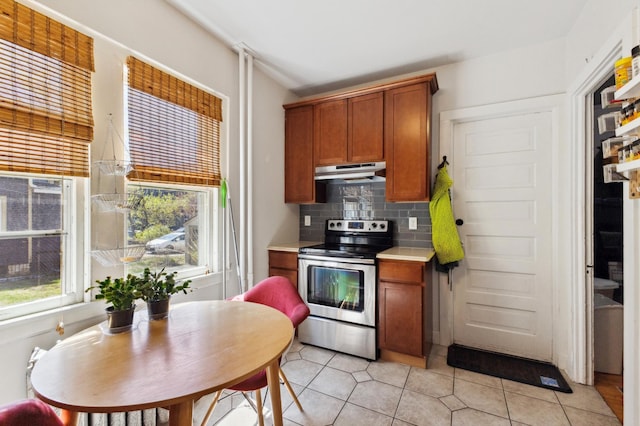 kitchen with brown cabinets, electric range, backsplash, under cabinet range hood, and light countertops