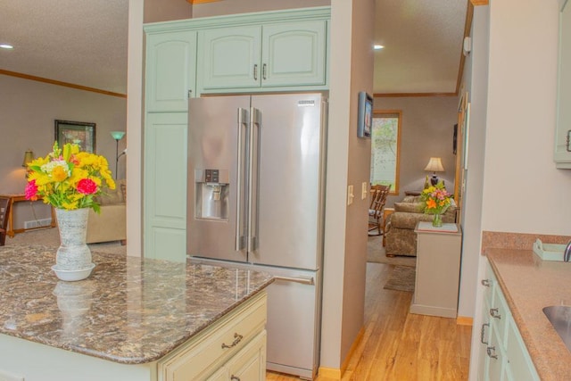 kitchen featuring high end refrigerator, ornamental molding, light wood finished floors, stone countertops, and a textured ceiling