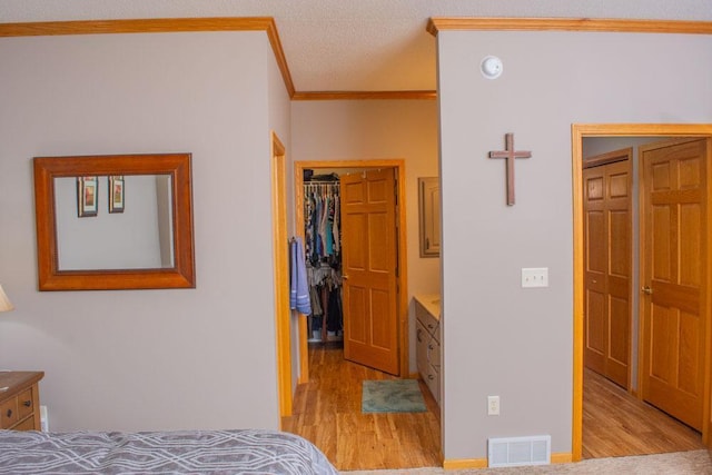bedroom featuring crown molding, light wood-type flooring, a spacious closet, and a closet