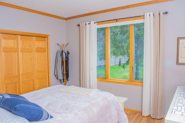 bedroom with multiple windows, light wood finished floors, crown molding, baseboards, and a closet