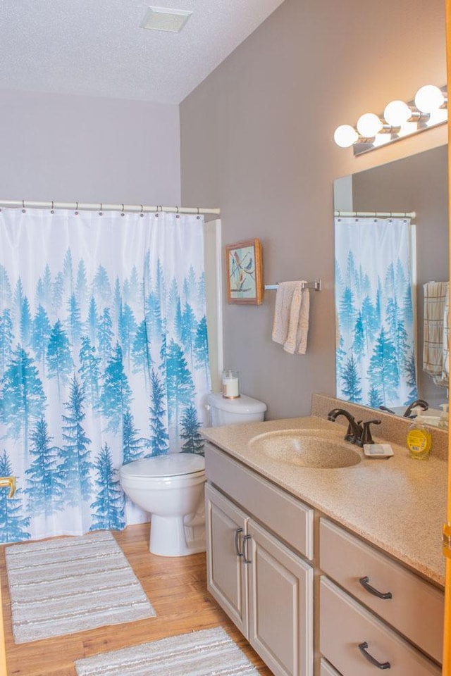bathroom with wood finished floors, toilet, vanity, curtained shower, and a textured ceiling