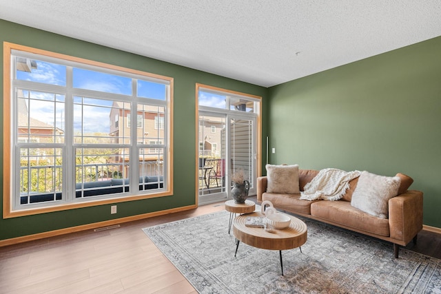 living area featuring a textured ceiling, visible vents, wood finished floors, and baseboards