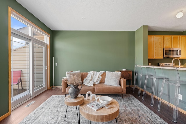 living area with a textured ceiling, baseboards, visible vents, and light wood-style floors