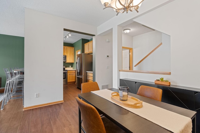 dining area with a textured ceiling, a notable chandelier, visible vents, and wood finished floors