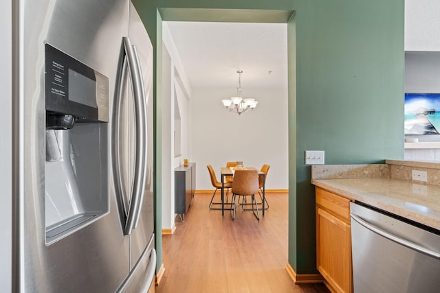 kitchen with light stone countertops, pendant lighting, an inviting chandelier, light wood-style floors, and appliances with stainless steel finishes