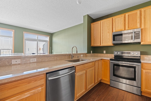 kitchen with a sink, stainless steel appliances, a textured ceiling, dark wood-style floors, and light brown cabinets