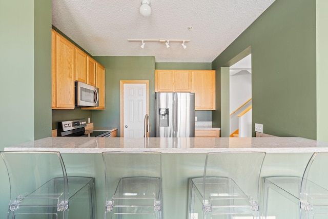 kitchen with a peninsula, a breakfast bar area, a textured ceiling, light countertops, and appliances with stainless steel finishes