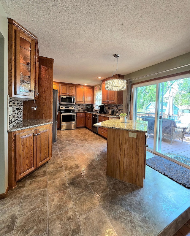 kitchen with stainless steel appliances, brown cabinets, a textured ceiling, backsplash, and a chandelier