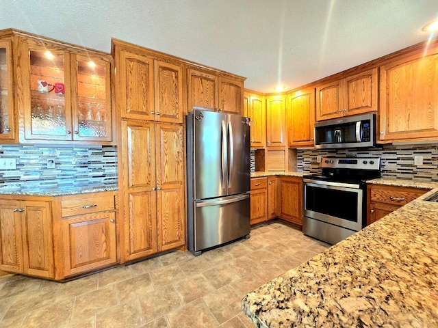 kitchen featuring stainless steel appliances, tasteful backsplash, light stone counters, and brown cabinetry