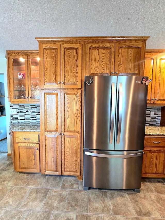 kitchen with freestanding refrigerator, brown cabinets, tasteful backsplash, light stone countertops, and a textured ceiling