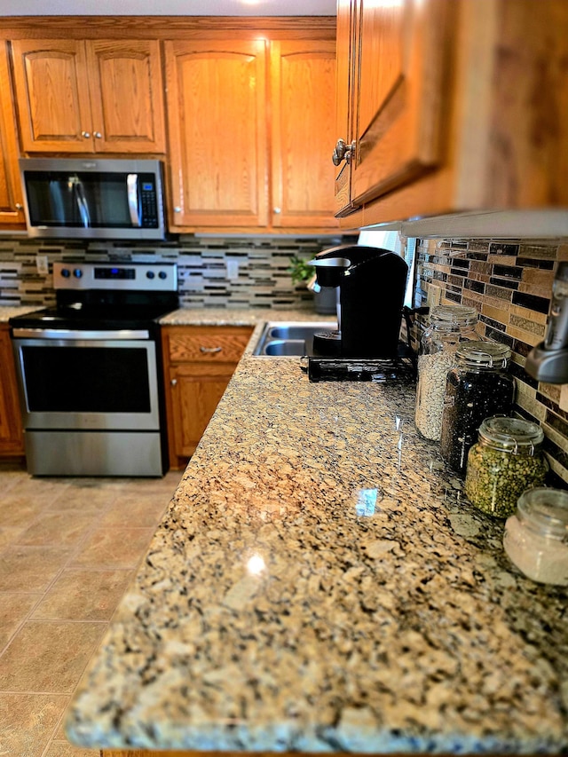 kitchen with stainless steel appliances, tasteful backsplash, brown cabinetry, and light stone counters
