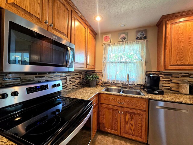 kitchen featuring stainless steel appliances, a sink, brown cabinetry, backsplash, and a textured ceiling