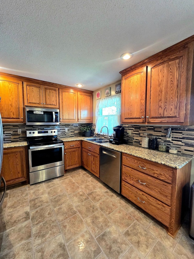 kitchen with appliances with stainless steel finishes, a sink, brown cabinets, backsplash, and a textured ceiling