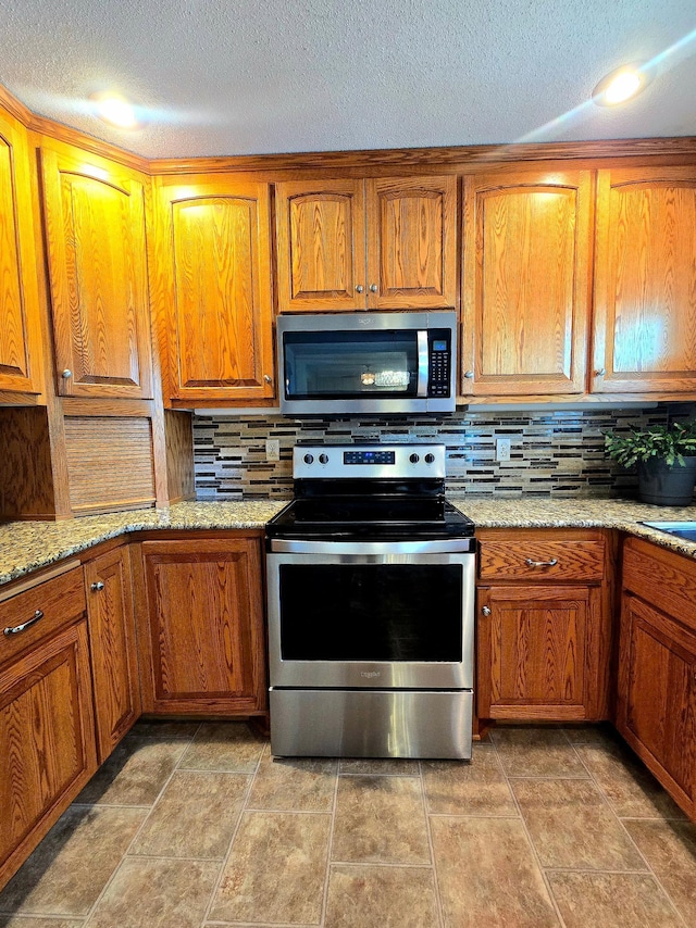 kitchen with stainless steel appliances, a textured ceiling, brown cabinetry, backsplash, and light stone countertops