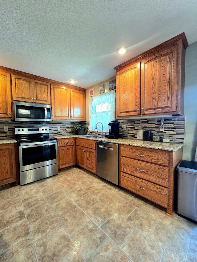 kitchen with appliances with stainless steel finishes, brown cabinetry, tasteful backsplash, a sink, and a textured ceiling