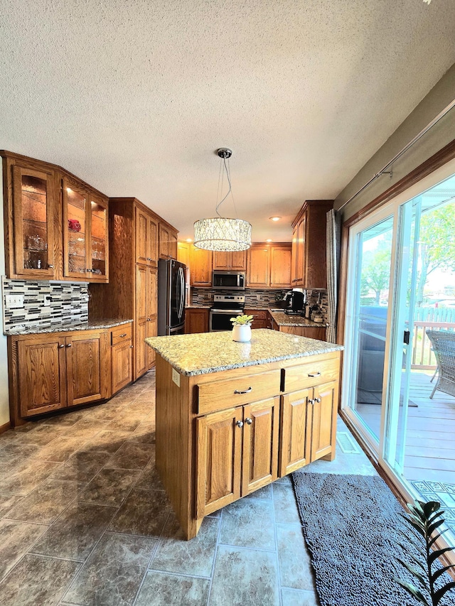 kitchen with appliances with stainless steel finishes, a kitchen island, tasteful backsplash, glass insert cabinets, and light stone counters