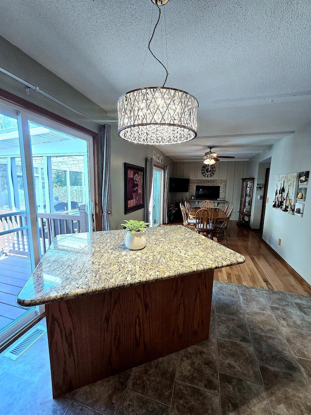 kitchen with a textured ceiling, ceiling fan, a kitchen island, light stone counters, and decorative light fixtures