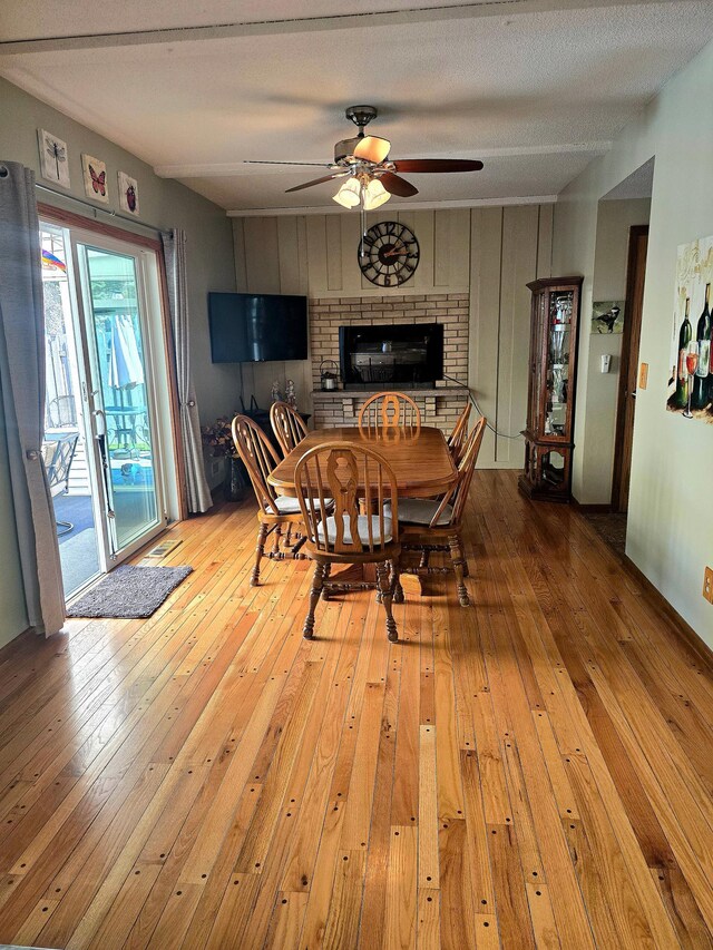dining room featuring light wood finished floors, ceiling fan, and a brick fireplace