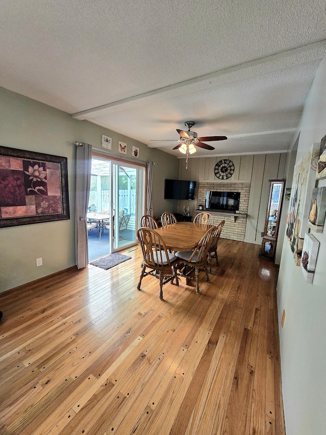 dining room with a ceiling fan, hardwood / wood-style floors, a textured ceiling, a brick fireplace, and baseboards