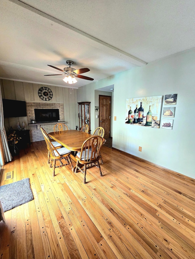 dining room featuring a brick fireplace, light wood finished floors, and a ceiling fan